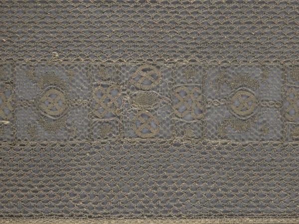 A so-called Saxon lace belt, lace belt and clothing accessory for men's fashion. The central part is a continuous belt with a geometric ornament; among the motifs is a circle containing an hourglass. Side belts of similar width are permanently connected. The entire belt is trimmed with fringe. 17th/18th century, Poland. Lace, clothing accessory; height 270 cm, width 25 cm., A close-up view of a textile with an intricate lace pattern showing a repeating horizontal band of decorative motifs between sections of a fine openwork mesh; the lace is made of a thread in a beige or tan color and sits over a background that appears grayish-blue, creating contrast; the horizontal decorative band contains a series of framed shapes with circular and diamond-like motifs and small woven fills, while the surrounding mesh consists of interlinked loops forming a net-like texture; overall the image shows an even, symmetrical arrangement of the beige or tan lace against the muted gray-blue background.