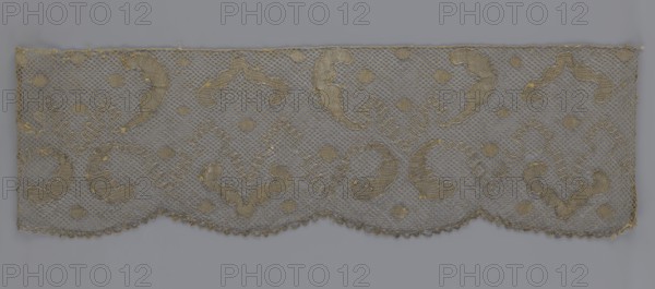 Lace fragment, lace, 18th century, Europe; fabric; width 20 cm, length 120 cm; purchased provenance., A rectangular piece of openwork fabric with a scalloped lower edge, showing a repeated ornate pattern of curving motifs and small diamond-shaped motifs on a net-like ground; the fabric appears in shades of gray and muted gold, with the net background in gray and the embroidered or woven decorative elements in gold and beige tones, and a few tiny flecks of darker gold scattered across the surface.