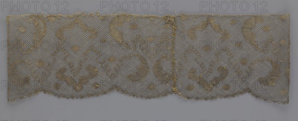 Lace fragment, lace, 18th century, Europe, fabric, width 20 cm, length 120 cm, A rectangular piece of delicate openwork fabric with a net-like ground and an embroidered scrolling pattern, shown against a plain background. The textile displays a scalloped lower edge and a straight upper edge, with an apparent seam or join near the center. The embroidery and net appear in muted tones of gold and beige, while the background surface beneath the textile shows a cool gray. The fabric has areas of slight fraying and a few loose threads along the edges and seam. The overall visual effect is a repeating ornamental design of curved paisley-like motifs and small round fills across the netted field.