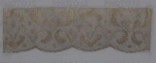 Lace fragment, lace, 18th century, Europe, lace fabric, width 20 cm, length 120 cm, A rectangular piece of sheer fabric with a scalloped lower edge displaying an ornate lace pattern, showing a mesh background interspersed with decorative motifs that include curved, paisley-like shapes and small rounded dots; the lace appears delicate with some areas showing slight fraying and tiny loose threads. The predominant colors visible are muted gray of the mesh and a metallic gold in the embroidered motifs, with subtle variations where the gold thread clusters appear denser or worn. The overall composition is horizontal, with repeating decorative elements across the width and a fine net-like texture filling the spaces between the motifs.