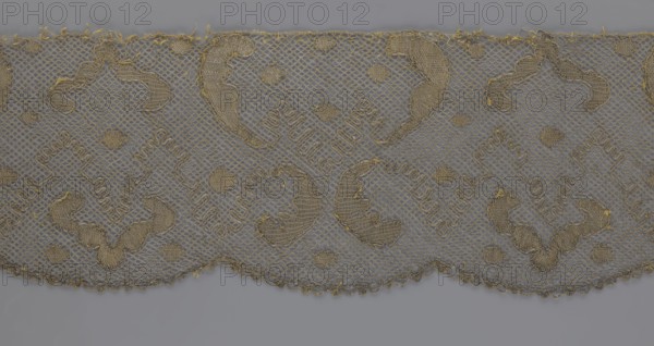 Lace fragment, lace, 18th century, Europe, fabric, width 20 cm, length 120 cm, purchased provenance, A scalloped piece of lace fabric with a repeating decorative pattern is shown against a neutral background; the lace is primarily golden tan with finer threads forming a net-like structure and thicker embroidered areas creating curved and diamond-shaped motifs, and the background appears gray.