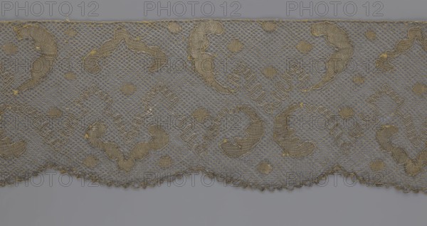 Lace fragment, lace, 18th century, Europe, lace fabric, width 20 cm, length 120 cm, A piece of lace fabric with a net-like background and a scalloped lower edge, featuring a repeating pattern of curved and diamond-shaped embroidered motifs in muted gold and tan threads against a soft gray background, with a few small embroidered dots and subtle variations in thread thickness and texture.