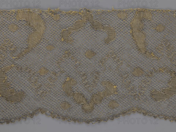 Lace fragment, lace, 18th century, Europe, lace fabric, width 20 cm, length 120 cm, A section of lace fabric with a netted background in gray and metallic gold threads forming an all-over pattern, showing a scalloped lower edge and a straight upper edge, with several larger solid embroidered motifs and a few smaller rounded filled motifs distributed across the surface, the embroidery creating textured raised areas and loose thread ends in places, overall colors visible are gray and gold.