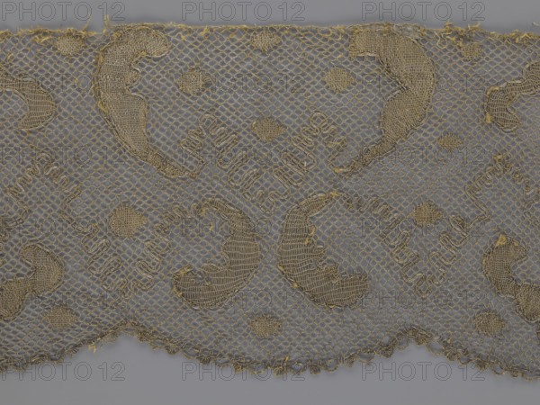 Lace fragment, lace, 18th century, Europe, fabric, width 20 cm, length 120 cm, A piece of fabric with a mesh-like net pattern in a gold color laid over a gray background, showing a repeating decorative motif of irregular rounded shapes and small circular patches woven with a denser stitch in the same gold tone, with scalloped lower edge and some loose thread ends; the overall colors visible are gold and gray.