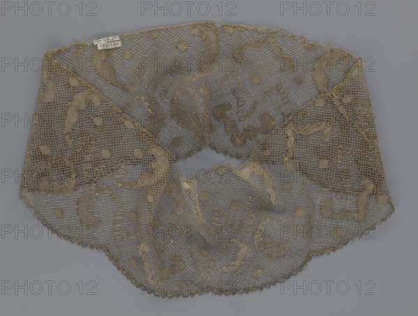 Lace fragment, lace, 18th century, Europe, fabric, width 20 cm, length 120 cm, A delicate lace collar made of an open net-like fabric is visible, laid flat against a gray background; the lace features a repeating organic motif with curved shapes and round dots in a muted golden-beige thread, and the netting and decorative elements share similar golden-beige tones while some areas appear slightly darker or more worn, showing variations in the beige and grayish-beige hues; the collar edge has a scalloped trim in the same golden-beige color, and the overall shape is semicircular with a central rounded opening.