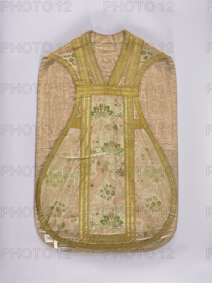 Chasuble, lace ornaments, floral ornaments, flowers, ribbons, liturgical vestments, plant ornaments, church paraments, sacred art, churches and chapels furnishings. The pattern is created by wavy ribbons with fan-shaped bouquets of small flowers surrounded by a serrated collar. The background is filled with small, curling flowers. The columns are trimmed with wide gold galloon; the edges of the chasuble are narrower. Linen lining, pink. 1st quarter of the 18th century, France. Liturgical vestment. Length 101 cm, width 66 cm back. Maker, A single ornate vestment displayed flat, shaped with a rounded lower edge and a narrower top opening, made of a lustrous beige silk ground with panels of patterned brocade; the brocade panels show floral and foliate motifs in pale green and soft pink on a light beige background, framed and edged by wide gold trim and narrow gold bands; the outer fabric appears a muted beige or tan with a subtle sheen, and the overall color palette includes beige, gold, ...