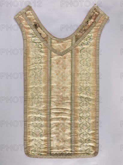 Back of a chasuble, creator unknown, origin unknown. Grosgrain chasuble with plant tendril ornament arranged in vertical stripes and a lace pattern featuring vines and flowers. Colors: cream background with sand and blue ornament. Trimmed with silver galloon. Front neckline pieced with a different silk fabric. Red cotton lining. 2nd half of the 18th century, France. Liturgical vestment. Back dimensions: length 134 cm, width 64.5 cm., A sleeveless garment laid flat against a pale background, shaped with a deep rounded neckline and long, rectangular body tapering slightly toward the top; the fabric shows a vertical striped pattern with alternating panels of muted gold, cream, and beige tones, some panels featuring floral damask designs in soft brown and green, and others with delicate scrolling floral motifs in pale green and blue; the neckline and edges are finished with a silvery-beige trim that has a slightly ribbed texture, and there is subtle wrinkling and signs of wear in places, e...