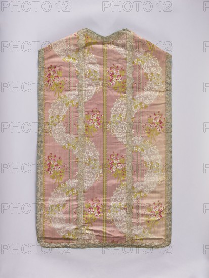 Chasuble, origin unknown, 2nd half of the 18th century, France. Light plum background with white, green, and cherry-red floral and plant ornaments—floral bouquets, flowers, and leaves—trimmed with silver lace; blue cotton lining. Liturgical vestment church/chapel furnishing, length 104 cm, width 62 cm back., A tall, rectangular textile panel with a pointed top, shown against a pale background, featuring a pink base with vertical ribbed texture and patterned stripes; the surface has ornate floral motifs in shades of white, yellow, green, and bright pink, arranged in flowing curved bands and clustered bouquets; there are several narrow vertical borders of metallic trim in a silvery-gold tone running down the length and framing the edges, with additional scalloped metallic edging in pale gold and silvery-blue along the outer perimeter; the overall palette includes pink, white, yellow, green, bright pink, silvery-gold, and pale blue.