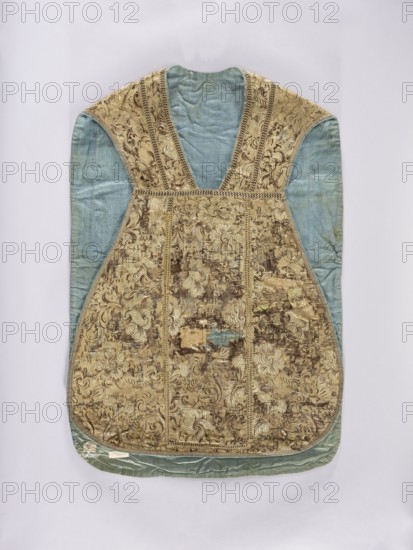 Chasuble, liturgical vestment, flowers and plant ornaments, church paraments, columns highlighted with narrow braid stitching with gold-brown darts. The edges of the chasuble are trimmed with gold-silver braid. Blue linen lining. 18th/19th century, France. Length 95 cm, width 64 cm back., A sleeveless garment photographed flat against a light background, showing a front panel with ornate patterned fabric in shades of gold and brown with a floral and scroll motif, bordered by braided trim; the sides and inner neck area are a faded blue-green silk, and the garment shows areas of wear and patches where the underlying blue-green fabric is visible; overall colors visible include gold, brown, blue-green, and small hints of darker brown.