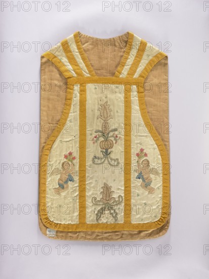 Chasuble, Liturgical vestment, 18th century, Poland. Front column embroidered with stylized flowers and angels; rear column: center figure of the Madonna on the moon; sides with angels holding flowers; background covered with tiny stars. Entire piece trimmed with smooth woolen braid. Predominant colors: white background with light pink, blue, and sand ornament. Linen lining. Dimensions: length 96 cm, width 61 cm back., A garment shaped like a sleeveless vest with a rounded top and curved sides is shown flat against a pale background, featuring a beige base with wide golden yellow trim forming vertical and shoulder bands; the front panels are a lighter cream color with embroidered decorative motifs including floral and foliate forms and a pair of cherubic figures holding small bouquets, rendered in muted tones of pink, blue, green, tan, and brown; the golden trim has a textured look, and the overall fabric shows slight creasing and a subtle sheen.