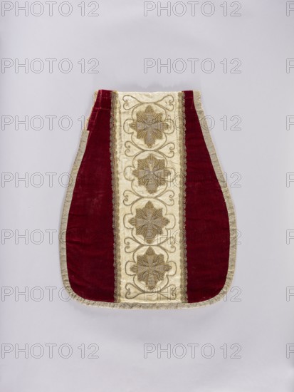 Chasuble, liturgical vestment, 18th–19th century, Poland. Back: sides of smooth dark red velvet. Column of white damask with floral patterns and braid and sewn-on stars from the Order of the White Eagle; on the stars the inscription Pro Fide Rege Lege. Six stars intended, one is missing. Embroidery between the stars with thin thread. Silver galloon. Cotton lining. Front: column of white damask covered with silver and gold thread embroidery featuring stars and crosses with a Latin inscription. Entire piece trimmed with silver braid. Four stars with the inscription Pro Fide Rege Lege. Damask with floral and braided patterns. Silver braid. Cotton lining. Length 122 cm; width back 64 cm., A tapered textile piece with a central vertical panel in a creamy color featuring a repeating floral motif in metallic tones, flanked by narrow decorative trim, and bordered on both sides by deep red velvet panels with a metallic outer edging; the background is pale gray and the visible colors include cre...