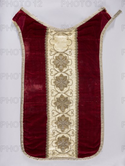 Chasuble, liturgical vestment, 18th–19th century, Poland. Back: sides of smooth dark red velvet; central column of white damask with floral patterns and braid and sewn-on stars of the Order of the White Eagle, bearing the inscription Pro Fide Rege Lege one of six stars is missing. Embroidery between the stars with thin thread; silver galloon; cotton lining. Front: central column of white damask covered with silver and gold thread embroidery featuring stars and crosses with a Latin inscription; trimmed with silver braid. Damask with floral and braided patterns. Length 122 cm, width 64 cm back., A single garment laid flat with a vertical design, featuring a central creamy panel with decorative raised motifs framed by metallic trim, flanked by wide deep red velvet panels and edged all around with a pale metallic border; the central panel contains a vertical sequence of ornate floral-like medallions in muted gold and beige with swirling embellishments, and the red velvet shows areas of she...