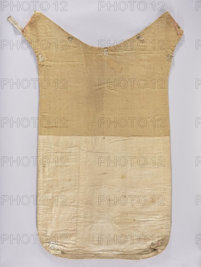 Chasuble, liturgical vestment, 18th–19th century, Poland. Back: sides of smooth dark red velvet. Column of white damask with floral patterns and braid and sewn-on stars of the Order of the White Eagle; on the stars the inscription Pro Fide Rege Lege. One of six stars missing. Embroidery between the stars with thin thread. Silver galloon. Cotton lining. Front: column of white damask covered with silver and gold thread embroidery featuring stars and crosses with a Latin inscription. Trimmed with silver braid. Four stars with the inscription Pro Fide Rege Lege. Damask with floral and braided patterns. Cotton lining. Length 122 cm, width 64 cm back., A flat, elongated textile laid vertically with a rounded lower edge and a curved upper section forming two angled extensions; the upper portion is a warm tan color while the lower portion is a lighter beige, and the background is a pale gray. The fabric shows visible creases and slight discoloration spots, with frayed edges at the upper extens...