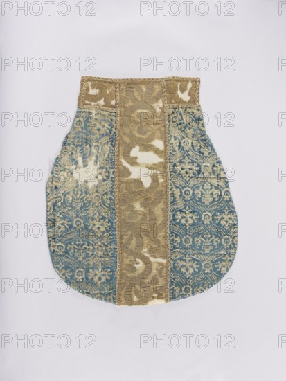 Chasuble, liturgical vestment decorated with flowers, leaves, and plant ornaments; church paraments, sacred art. Chasuble of Genoese velvet, patterned, convex, with a regularly repeating motif of a stylized bouquet of flowers in vases enclosed in a thick heart-shaped net; mesh fastened with palmettes. Colors: sapphire blue ornament on cream-gold background; columns of solid material in gold-beige. Ornamentation on fabric is not fully legible due to large defects. Made of stylized plant forms. 15th/16th century; possibly Italy or France, sides: Genoa. Length 122 cm, width 64 cm back., An object resembling a shaped textile panel lies flat against a pale background; it has a rounded lower body with a narrower rectangular top and is made from patterned fabric with a central vertical strip in a muted gold color flanked by two wider blue panels featuring an ornate repeating floral and scroll motif, with areas of lighter worn patches on both the gold and blue fabrics; the top edge includes a ...
