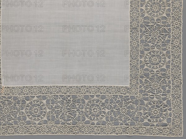 Doily, geometric ornaments, rosettes ornament, doilies. Smooth center. Edge made of white linen lace with rosette motifs: large rosettes in the center and rows of small rosettes on the edges, punto in tela lace, ca. 1600, Italy. Materials: lace, fabric. Height 79 cm, width 70 cm., A corner of a fabric piece with a plain central area and a decorative openwork border, showing a few shades of off-white and light beige fabric against a muted gray background; the plain area is smooth and slightly textured while the border consists of intricate lace-like patterns with circular and geometric motifs and fine threadwork.