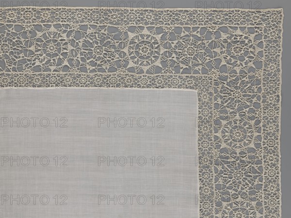 Doily, smooth center. Edge made of white linen lace with rosette motifs: large rosettes in the center and rows of small rosettes on the edges; punto in tela lace; ca. 1600, Italy. Materials: lace, fabric. Dimensions: height 79 cm, width 70 cm. Style/details: geometric ornaments, rosettes ornament, doily., A section of a rectangular fabric with a plain central panel in a light gray or off-white color bordered by an intricate lace edging in a creamy beige tone, the lace featuring repeating geometric and floral-like openwork motifs with circular and star-shaped patterns, thin connecting threads, and a narrow band of denser lace separating the central panel from the wider outer lace border; the background behind the lace appears as a medium gray surface.