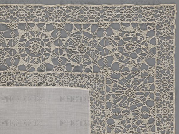 Doily, geometric ornaments; rosettes ornament; doilies; smooth center. Edge made of white linen lace with rosette motifs: large rosettes in the center and rows of small rosettes on the edges; punto in tela lace; ca. 1600, Italy; lace fabric; height 79 cm, width 70 cm., A close-up view of a corner of a rectangular textile featuring a solid woven central panel in a pale off-white color bordered by an intricate openwork lace in a slightly warmer creamy off-white; the lace displays repeating geometric and circular motifs connected by delicate looping threads, with visible small open spaces throughout, and the background beneath the lace appears as a muted medium gray.