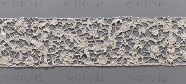 Lace fragment, needle lace with floral ornaments, pattern of large, thick branches with stylized flowers and leaves; details executed in relief; joints rare with rosettes snowflakes. 2nd half of the 19th century, Italy. Lace fabric, width 15 cm, length 248 cm., Purchase, A horizontal strip of openwork lace with an intricate floral and scroll pattern laid flat against a solid background; the lace appears off-white or cream with visible textured stitching and raised embroidered elements forming flowers, leaves, loops, and curving tendrils connected by delicate bridgelike threads, and the background is a uniform medium gray.