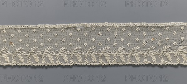 Fragment of lace, Alençon lace decorated with small twigs in projections and a tendril with feathery leaves running parallel to the edge against a mesh background; 2nd half of the 18th century, France, lace; width 8.5 cm, length 58.5 cm., A horizontal strip of delicate lace in off-white spans the image against a flat gray background, with a pattern of small embroidered floral motifs on a fine hexagonal mesh above a band of more densely stitched leafy vine designs; the lace edge shows a scalloped trim and a few loose threads, and there are a few small darker brown spots on the fabric.