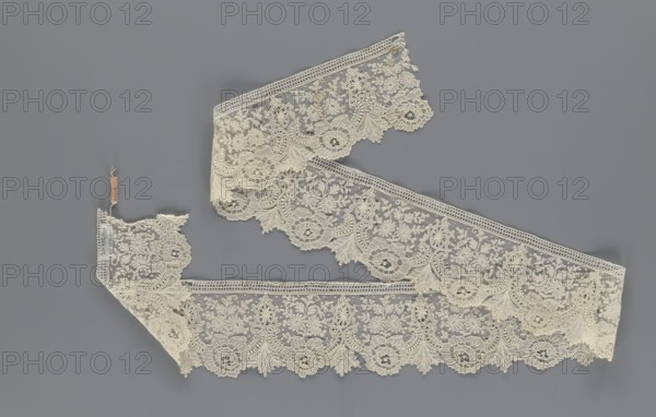 Lace fragment, lace, plant ornaments. Serrated on one side, with a pattern of flowers, fan-shaped leaves, and ovoid rosettes above them. Rose flowers between the leaves, and sprigs of other small flowers above them. Background fond de gaze. 2nd half of the 19th century, Brussels, lace, width 8.5 cm, length 127 cm, A length of delicate lace trim displayed against a gray background, the lace is an off-white or cream color with intricate floral and ornamental patterns, scalloped edges, and a fine mesh ground; several sections are arranged in a loose zigzag, with a few small attached tags visible at one end; the design shows repeating round floral motifs, leafy sprays, and ornamental scrolls, with textured raised embroidery and openwork areas.