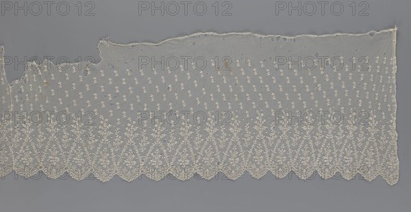 Lace fragment — shuttlecock;, mid-19th century France. Lace shuttlecocks; clothing accessory for fashion. Lower edge: semicircular serrations bordered with fine serrations with geometric ornament. From the semicircular serrations upwards: repeating floral ornament with a twig motif in triangular divisions; above this, a small twig in a regular projection. Lace; width 42 cm, length 430 cm., A long piece of delicate lace fabric laid flat showing an intricate repeating embroidered floral pattern with a scalloped lower edge; the lace is mainly off-white and cream with areas of slight discoloration, set against a smooth gray background; the fabric has a fine netted ground with a few irregular holes and some frayed edges along the top, and the embroidery forms denser floral motifs along the bottom that become more sparse toward the top.