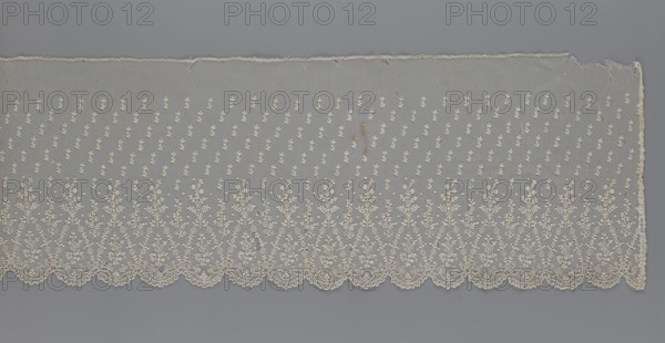 Lace fragment — shuttlecock;, Mid-19th century, France. Lace shuttlecocks, clothing accessories; fashion. Lower edge: semicircular serrations bordered with fine serrations with geometric ornament. From the semicircular serrations upwards: a floral ornament repeating with a twig motif in triangular divisions. Above this, a small twig in a regular projection. Dimensions: width 42 cm, length 430 cm., A long piece of delicate lace fabric laid flat against a gray background, primarily cream or off-white in color, with a scalloped lower edge and a straight upper edge that shows some fraying; the lace has a repeating pattern of small floral motifs across the field and larger, more intricate floral sprays rising from the scalloped border, with visible tiny holes and a few small darker discolorations in the fabric; the background behind the lace is a smooth mid-gray.