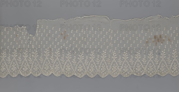 Lace fragment - shuttlecock, mid-19th century, France; lace; clothing accessory shuttlecock; lower edge with semicircular serrations bordered by fine serrations with geometric ornament; above semicircles a repeating floral ornament with a twig motif in triangular divisions; above this a small twig in a regular projection; width 42 cm, length 430 cm., A length of delicate lace fabric laid flat against a solid background, showing a scalloped lower edge with intricate floral embroidery and repeating ornate motifs above; the lace is predominantly off-white or cream with small embroidered leaf-like patterns across the body and denser floral designs along the scalloped border, and there are a few irregular holes and tears near the top edge as well as some small brownish stains scattered in several spots; the background behind the lace is a uniform cool gray.