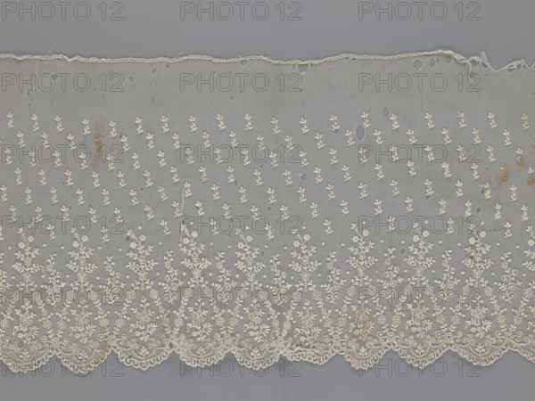 Lace fragment - shuttlecock;, purchase, Lace shuttlecocks used as clothing accessories and fashion. Lower edge: semicircular serrations bordered with fine serrations with geometric ornament. From the semicircular serrations upwards: floral ornament repeating with a twig motif in triangular divisions. Above this: a small twig in a regular projection. Mid-19th century, France. Material: lace. Width 42 cm, length 430 cm., A length of delicate lace fabric laid flat showing a sheer gray background with an overall pattern of small floral motifs embroidered in off-white or cream, a scalloped embroidered lower edge with denser, more intricate floral and vine designs, a worn upper edge with fraying, several small holes and irregular open areas scattered across the fabric, a few faint brownish stains, and subtle variations in thread texture and density.