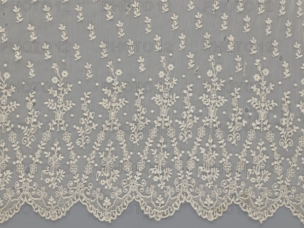Lace fragment — shuttlecock; mid-19th century, France. Lace shuttlecocks, clothing accessories, fashion. Lower edge: semicircular serrations bordered with fine serrations with geometric ornament. From the semicircular serrations upwards: a floral ornament repeating with a twig motif in triangular divisions; above this, a small twig in a regular projection. Material: lace. Width 42 cm; length 430 cm., A continuous length of sheer fabric with an overall pale cream embroidery against a muted gray background, featuring a repeating floral and vine motif with a scalloped embroidered edge; the design shows several vertical sprays of small leaves and blossoms, a few dotted accents scattered throughout, and a group of tiny mesh openings in the ground fabric.
