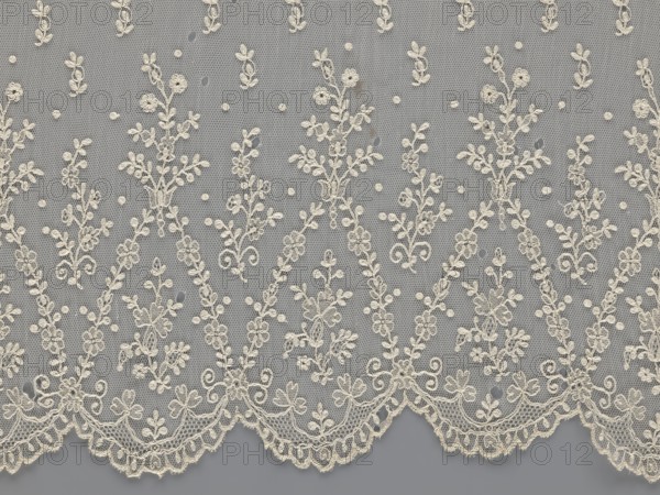 Lace fragment - shuttlecock;, mid-19th century, France. Lace shuttlecocks, clothing accessories, fashion. Lower edge: semicircular serrations bordered with fine serrations with geometric ornament. From the semicircular serrations upwards: a repeating floral ornament with a twig motif in triangular divisions; above this, a small twig in a regular projection. Materials: lace. Dimensions: width 42 cm, length 430 cm., A length of delicate lace fabric with an overall beige or off-white embroidered floral pattern set against a gray background, showing a repeating design of vertical vine-like motifs with small flowers and leaves connected by dotted netting, and a scalloped lower edge featuring denser floral embroidery and ornamental loops.