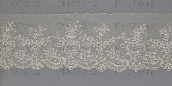 Lace fragment - shuttlecock;, Fashion accessory; needle lace and bobbin lace; shuttlecocks; tiny spiders—needlework and bobbin ornament elements on factory-made tulle. Floral ornament with a large repeat. Serrated lower edge with stylized feathery leaves and flower calyces; above them are floral bouquets and flower projections. 1st half of the 19th century, France. Lace. Width 39 cm, length 328 cm., A length of delicate lace fabric laid flat, featuring an intricate floral and foliate pattern embroidered onto a sheer net background; the lace displays a scalloped lower edge with ornate swirls and loops and a straight torn upper edge, and the embroidered motifs include bouquets, leafy sprigs, and clustered blossoms connected by sinuous stems. The visible colors are off-white or cream for the lace and a muted gray background behind the sheer net.