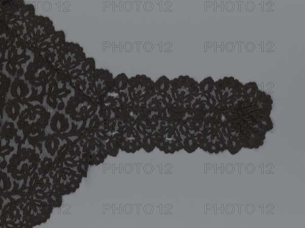 Cape, lace, in the form of a square with two wide, elongated lace ties. Continuous floral ornament with a motif of a large, asymmetrical flower sprig. Raised edge with a strip of floral edge ornament made separately and sewn on. 2nd half of the 19th century, France. Height 97 cm, width 168 cm. Maker: unknown., A length of black lace fabric with a floral pattern lies against a smooth gray background, showing scalloped edges and intricate openwork with a few overlapping sections and a long narrow extension; the visible colors are black and gray.