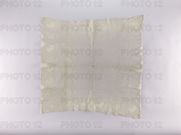 Cope by, embroidered ornament with a continuous form alternating between large flowers and feathery leaves; on the slightly shorter central edge the ornamental band is doubled. 19th century, Silesia. Liturgical vestment church parament, decorated with plant ornaments—flowers and leaves. Height 102 cm, width 103 cm., A square, light-colored fabric laid flat against a pale background, showing a decorative border of looping, fern-like embroidery along two adjacent edges and partially along the opposite edges; the fabric itself is a soft off-white or cream with slightly darker cream embroidery, visible fold lines and gentle wrinkles, and subtle shadowing around the edges.