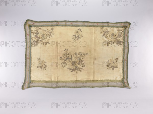 Wall hanging of rep fabric sewn from many fragments, embroidered with beige, cream, ash, and brown silk thread with flat stitches, and with silver thread and plate with laid stitches — in places on a backing of thin string. In the center of the lower edge and in the upper corners are bouquets composed of large and small flowers, fruit, and cornucopias. In the lower corners and in the center of the upper edge are smaller floral sprigs. Trimmed with a wide mesh ribbon with sewn-on flowers. Tie strings are sewn onto the narrow edges. Floral motifs; plant ornaments; sacred art; churches and chapels furnishings. Piece width 49 cm, 23 weft threads and 35 warp threads per cm; brown selvedges; similar fabric density. 2nd half of the 18th century, Poland; fabrics. Height 73 cm, width 120 cm., A rectangular textile with a pale beige central panel featuring a few floral motifs in muted brown and gray tones, surrounded by a woven border in green and blue with small accents of pink and gold, the fa...