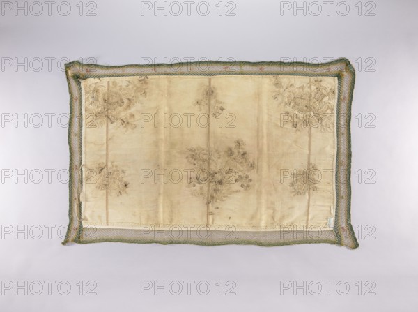 Wall hanging of rep fabric sewn from many fragments, embroidered with beige, cream, ash, and brown silk thread with flat stitches, and with silver thread and plate with laid stitches — in places on a backing of thin string. In the center of the lower edge and in the upper corners are bouquets composed of large and small flowers, fruit, and cornucopias. In the lower corners and in the center of the upper edge are smaller floral sprigs. Trimmed with a wide mesh ribbon with sewn-on flowers. Tie strings are sewn onto the narrow edges. Floral motifs; plant ornaments; flowers and leaves; sacred art; churches and chapels furnishings. Piece width 49 cm; fabric density 23 weft threads and 35 warp threads per cm; brown selvedges; height 73 cm; width 120 cm; 2nd half of the 18th century; Poland., A rectangular embroidered fabric panel lies flat against a light background, framed by a loosely woven border with a braided texture; the panel center is a pale beige or ivory silk with visible creases a...