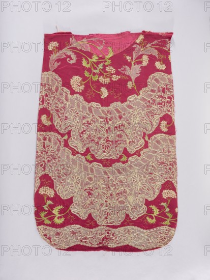 Back of a chasuble. Fragment of red amaranth satin fabric, embroidered; originally likely intended for the back of the chasuble as suggested by the fabric shape. Embroidery pattern imitates wide lace with a floral ornament distributed in two semicircular and one meandering stripe. Between the lace stripes are tall, curved branches with bird cherry flowers. Embroidery worked in silk yarn using split stitch, satin stitch, laid stitch, cord, and knots. 18th century, possibly Poland/ Germany/ France. Liturgical vestment. Width: 50 cm; overall length 100 cm, width 65 cm., A single rectangular textile panel with a rounded bottom displayed on a light background, predominantly deep pink in color with a few areas of bright green and pale cream lace-like embroidery; the surface shows an intricate floral and leaf pattern with clusters of rounded flower shapes and swirling leafy stems in green and cream, and extensive scalloped lace motifs in cream covering much of the center and lower portions, c...