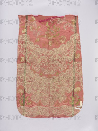 Back of a chasuble. Fragment of red amaranth satin fabric, embroidered; originally probably intended for the back of the chasuble, as suggested by the shape. Embroidery pattern imitates wide lace with a floral ornament distributed in two semicircular and one meandering stripe. Between the lace stripes are tall, curved branches with bird cherry flowers. Embroidery in silk yarn using split, satin, laid stitch, cord, and knots. 18th century, possibly Poland/ Germany/ France. Liturgical vestment. Width 50 cm; overall length 100 cm, width 65 cm., A rectangular piece of fabric with rounded bottom corners lies flat against a pale background, showing a dominant dusty rose color with a delicate overlay of pale cream lace-like embroidery forming ornate floral and scroll patterns across most of the surface; there are accents of light green embroidery in floral motifs scattered throughout, and narrow vertical stripes in darker green and a deeper pink run near the sides; the top edge appears slight...