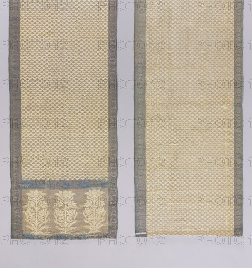 Kontusz belt, Tulips; double-sided, semi-solid triple-section heads with stylized tulip flowers and alternating boat motifs; floral tendril border; double triangle borders; geometric and plant ornaments. Right side: silver background, white ornament on heads and central part, navy blue borders; left side is the reverse. Unsigned; type associated with Istanbul/Constantinople belts—edge weaving and double-triangle motif characteristic of Armenian belts; making method similar to Constantinople examples; similar to a French or Gdodno belt with the same bush-and-flower motif. First half of the 18th century. Poland culture. National costume accessory. Length 268 cm; width 32 cm., A pair of long rectangular textile panels displayed side by side on a pale background, both panels showing an overall cream-colored ground with a repeating small-scale scalloped or scale-like pattern and narrow blue-gray decorative borders along their long edges, the left panel having a wider lower section with a ba...