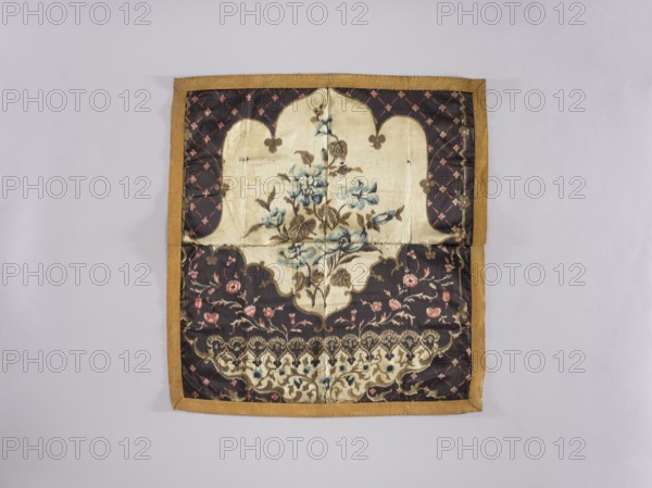 Tablecloth; maker, church paraments; printed fabric with flowers, leaves, and plant ornaments; sacred art for churches and chapels furnishings; 19th century; material: fabric; height 63.5 cm, width 59.8 cm, A square fabric panel with a golden brown border lies flat against a light gray background, showing a central cream-colored cartouche containing a floral motif in muted blue and brown tones, surrounded by a dark brown field patterned with small pink floral elements and lattice-like accents, with additional cream and brown decorative bands and a scalloped border design near the bottom.