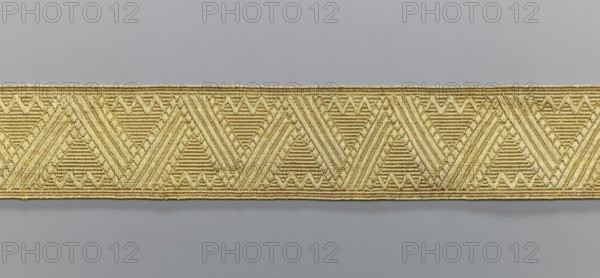 Gallon, origin unknown, galloons haberdashery, geometric ornaments, smaller snake pattern at the edges, early 19th century, Europe, fabrics, width 4.7 cm, length 53 cm, A horizontal strip of woven trim with a repeating geometric pattern sits against a smooth background; the trim shows a series of triangular motifs formed by tightly woven ridged lines and small raised accents, creating a textured surface with diagonal and horizontal linear detailing, and the visible colors are gold and gray.