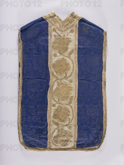 Chasuble, 17th century, Poland. Liturgical vestment. The sides are made of semi-silk navy blue damask 19th-century fabric with a motif of twisting floral sprigs. Columns have a tendril motif with schematic tulips and roses, embroidered with metal thread: silver in the background, gold in the ornamental sections. Edges and internal divisions trimmed with metal galloon. Cotton lining. Embroidery: gold metal thread on thick linen canvas backing. Background, leaves, and buds executed in flat laid embroidery; flower cups and stems in raised laid embroidery on a backing of linen threads. Gold threads consist of gold-colored metal plate ornamental parts and silver-colored metal plate background woven on a linen base; threads attached with linen yarn. Dimensions: length 114 cm, width 66 cm back., A vestment-like textile with a central vertical panel of metallic gold fabric featuring textured circular floral motifs bordered by narrower gold trim, flanked on both sides by deep blue panels patter...