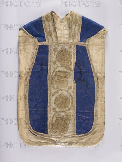 Chasuble, gift; tulips, plant ornaments, floral ornaments, flowers; liturgical vestment church paraments, sacred art, 17th century, Poland. The sides of the chasuble are made of a semi-silk navy-blue damask fabric with a motif of twisting floral sprigs. The columns have a tendril motif with schematic representations of tulips and roses, embroidered with metal thread: silver in the background, gold in the ornamental section. The edges and internal divisions are trimmed with metal galloon. Cotton lining. Embroidery: gold metal thread laid on a backing of thick linen canvas. Background, leaves, and buds — flat laid embroidery; flower cup and stems — raised laid embroidery on a backing of linen threads. Gold threads: gold-colored metal plate in ornamental parts and silver-colored metal plate background woven on a linen base; threads attached to the base with linen yarn. Length 114 cm, width 66 cm back., A garment laid flat with a long rounded bottom and a V-shaped neckline, showing a centr...