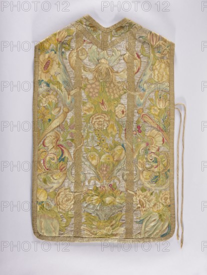 Chasuble, provenance unknown. Embroidered chasuble with birds, flowers, and fruit ornament; liturgical vestment used as a church parament. On a silver background, a multicolored pattern composed of a fruit vase, floral scrolls, grapes, and birds. Predominant colors: silver background and green, blue, and yellow ornament. Edges trimmed with gold braid with a geometric pattern. Internal divisions marked with strips embroidered with gold thread, imitating haberdashery. Cotton lining. Embroidery on linen canvas with multicolored silk and metal threads in two types: silver silver plate woven on a white silk base and gold gold plate woven on a yellow silk base. Metal thread embroidery in a laid flat stitch; colored embroidery in split, flat, and knot stitches. 18th century, Poland. Length 105 cm, width 64 cm back., An ornate textile panel with a pointed top and rounded bottom displayed against a light background, featuring an overall palette of gold, pale yellow, soft green, muted blue, crea...