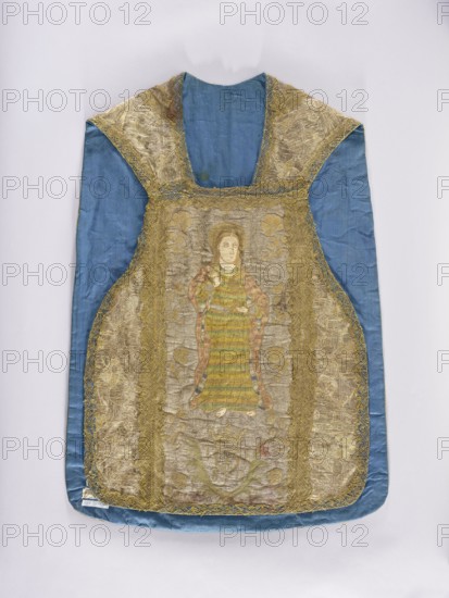 Chasuble, Madonna and Child, St. Bridget 1303–1373, Slepowron coat of arms, coats of arms, religious scenes, saints, floral ornaments, flowers, liturgical vestments, plant ornaments, church paraments, sacred art, churches and chapels furnishings. Chasuble made of solid fabric with a floral pattern, with embroidered columns. On the front column is the figure of St. John the Evangelist holding a chalice with a snake; below is a cartouche with the Slepowron coat of arms, around the cartouche the letters TLSD. On the back column is Mary and Child on a crescent; below is a kneeling Saint Bridget with an inscription around her head: SM BRI/GITTA. Stylized floral motifs embroidered in the background of the columns. The columns and sides of the chasuble are trimmed with gold bobbin lace. 17th century, Spain fabric?, Poland embroidery?. Liturgical vestment. Length 100 cm, width 69 cm back., A garment laid flat against a pale background, predominantly blue with a sheen to the fabric, featuring a...