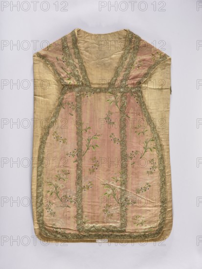 Chasuble, liturgical vestment;, noted. A large floral pattern and lace motif are set against a raspberry background. The dominant colors in the ornament are brown, silver, and green. The entire piece is trimmed with period lace. Divided into columns with sewn-on gold lace. 2nd half of the 18th century, Lyon, France. Liturgical vestment. Length 99 cm, width 66 cm back., A sleeveless garment laid flat with a rectangular body and a V-shaped neckline, made of a pale gold fabric with a central panel in a muted pink tone that features vertical stripe textures and a floral pattern; the pink panel is bordered by a scalloped trim in a metallic gold color, and the floral motifs include green leaves and small blue accents; the shoulder and side sections are pale gold matching the outer fabric, and the overall piece shows gentle creases and soft folds against a light neutral background.