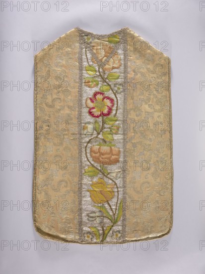 Chasuble, Floral and plant ornaments with flowers and leaves; columns embroidered on a silver background with large flower motifs in yellow, cherry red, green, and blue. Unstitched and trimmed with silver lace braid; cotton lining. Side fabric: cream silk brocaded with gold thread with stylized twigs and leaves. France, 3rd quarter of the 17th century fabric; 18th century, Poland embroidery. Liturgical vestment. Length 101 cm, width 67 cm back., A rectangular textile panel with a pointed top edge displayed against a pale gray background, featuring a central vertical embroidered panel with a winding stem bearing a group of stylized flowers and leaves, surrounded by a patterned brocade field; colors visible include gold and beige in the background fabric, green in the leaves, yellow and orange in some flower petals, pink and red in a central flower, and silver-gray in the narrow vertical band framing the floral embroidery.