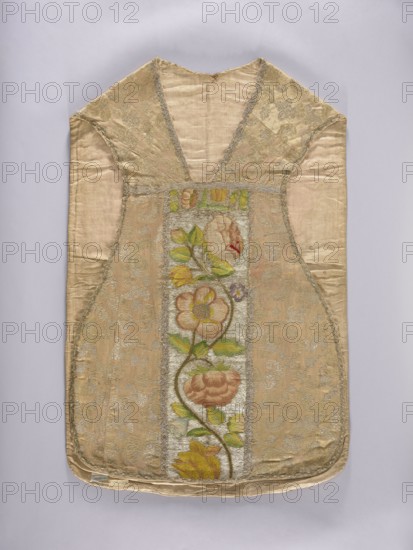 Chasuble, Floral and plant ornaments—flowers and leaves—embroidered in columns on a silver background with motifs of large flowers in yellow, cherry red, green, and blue. Chasuble unstitched and trimmed with silver lace braid; cotton lining. Side fabric: cream silk brocaded with gold thread with motifs of stylized twigs and leaves. France, 3rd quarter of the 17th century fabric; embroidery dated 18th century, Poland. Liturgical vestment. Dimensions: length 101 cm, width 67 cm back., A sleeveless garment laid flat with a deep V-shaped neckline, made of a pale beige fabric with a subtle sheen and patterned metallic brocade panels; a central vertical floral panel features a winding stem with stylized blossoms and leaves in shades of green, yellow, peach, and muted pink on a lighter background; the brocade sections on either side show pale silver and gold metallic motifs against the beige ground; the garment edges are finished with a narrow trim and the overall shape tapers toward the hem,...