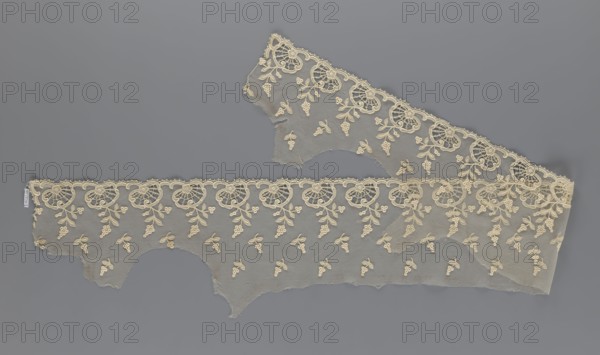 Fragment of lace, lace, plant ornaments, slightly serrated lower edge with shell motifs and sprouting twigs, above it projections of smaller twigs, 2nd half of the 19th century, Europe, lace, width 20 cm, length 161 cm, A length of delicate lace fabric laid flat on a gray background, showing a scalloped decorative edge and floral motifs worked into a fine net ground; the lace appears in shades of cream and off-white against the medium gray backdrop, with a repeating pattern of circular floral rosettes along the scalloped border and small clustered floral sprays scattered across the mesh, and with irregular torn edges and a few overlaps where the lace layers cross.