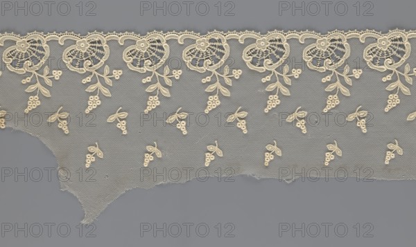 Fragment of lace, lace with plant ornaments, slightly serrated lower edge, shell motifs with sprouting twigs and projections of smaller twigs above, 2nd half of the 19th century, Europe, lace, width 20 cm, length 161 cm, A length of delicate lace fabric with an open mesh background in gray and cream hues, featuring a scalloped top edge with a repeating floral motif in cream; dangling from the scalloped border are cream embroidered leaf-and-berry sprigs, and a scattered pattern of small cream berry-and-leaf clusters fills the mesh area; the lower edge is irregular and frayed, and the overall colors visible are gray and cream.