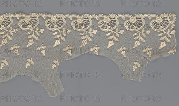 Fragment of lace, lace with plant ornaments, slightly serrated lower edge with shell motifs and sprouting twigs, above it projections of smaller twigs; 2nd half of the 19th century, Europe; lace, width 20 cm, length 161 cm., A delicate piece of netted fabric with an embroidered scalloped top edge in an off-white or cream color laid against a flat gray background, showing a repeating floral and vine motif along the upper border with smaller clustered berry-and-leaf designs scattered below; the netting has a fine diamond mesh and irregular torn lower edges, and the embroidery stitches and raised threadwork create subtle texture and shadow on the cream and gray surfaces.
